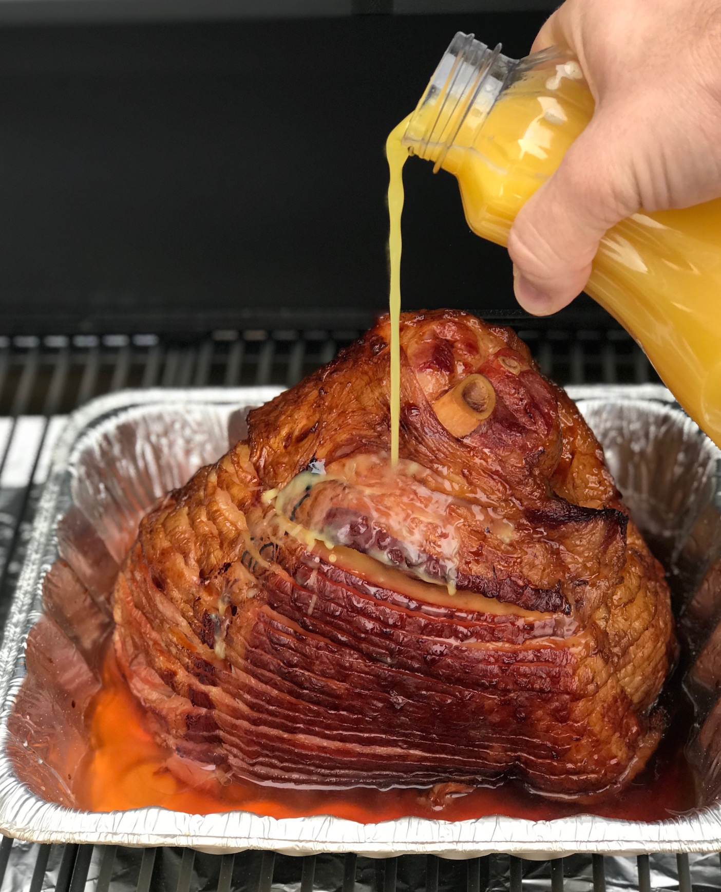 Smoked ham getting some orange juice poured on it during the cooking process.
