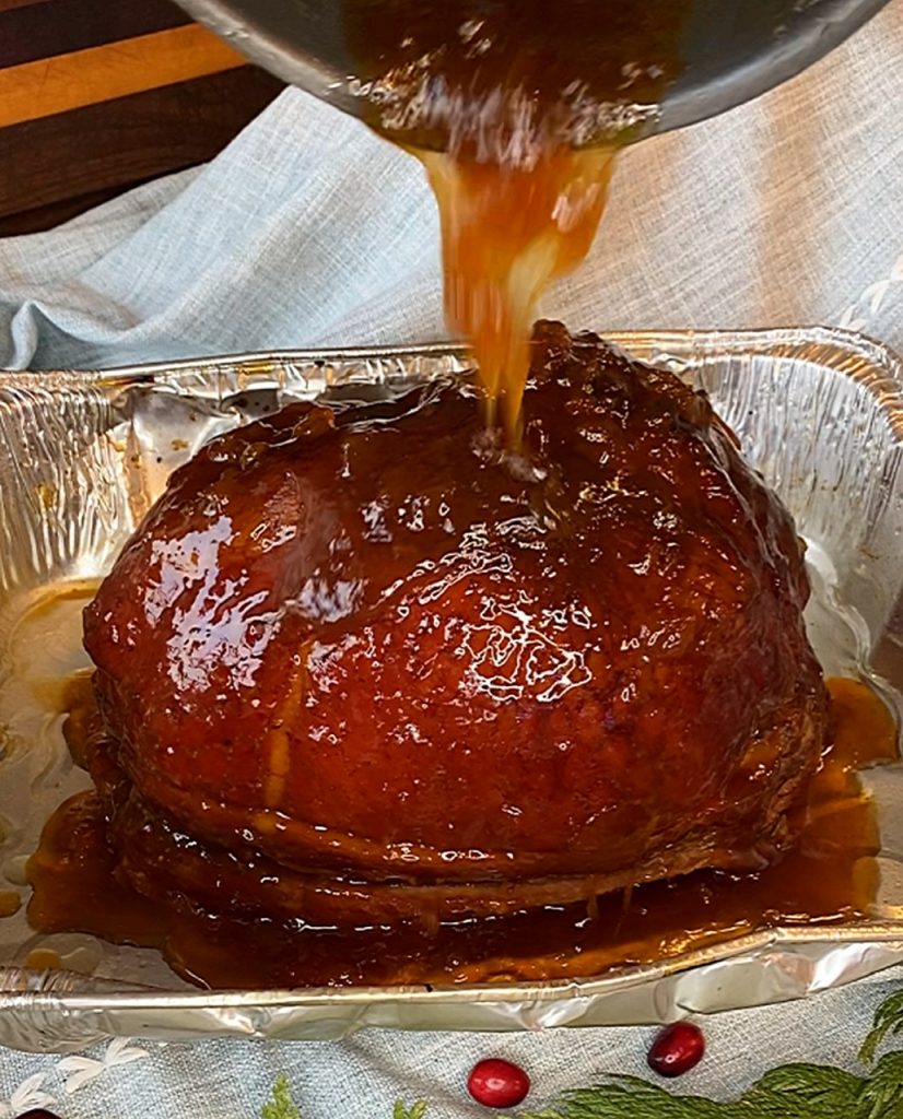 Cinnamon apricot glaze cascading down the smoked ham in a foil pan.