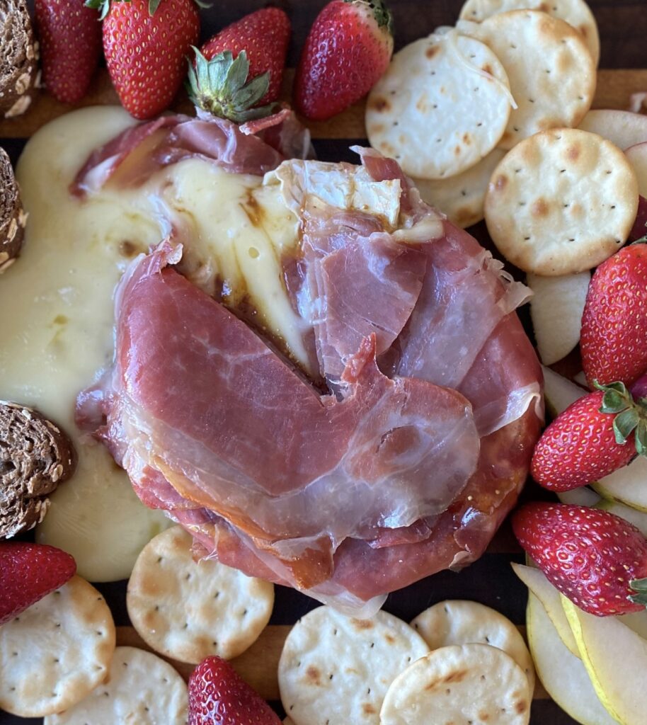 Smoked prosciutto wrapped Brie served with baguette, crackers, strawberries, and apples. 