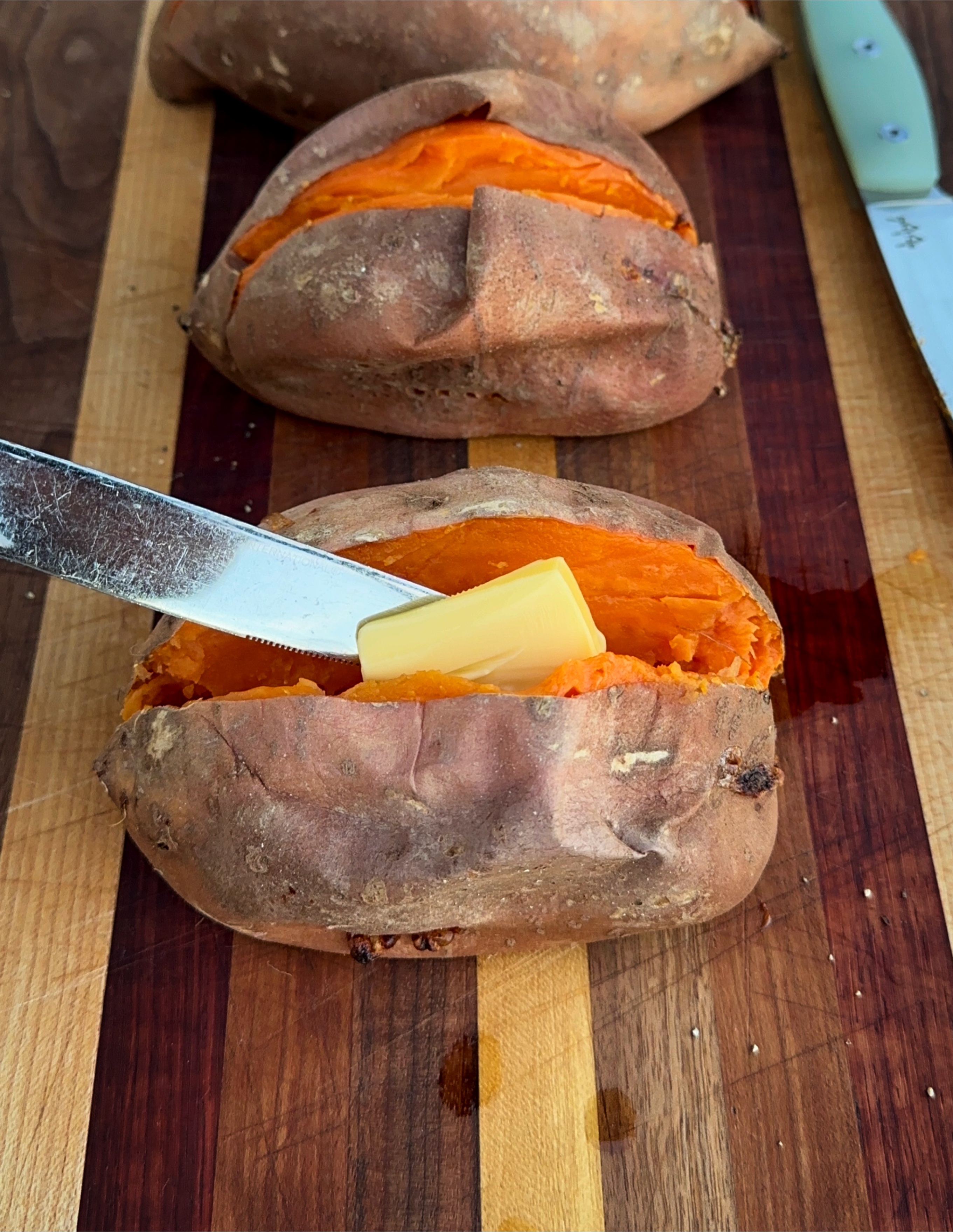 Grilled sweet potatoes being topped with butter. 