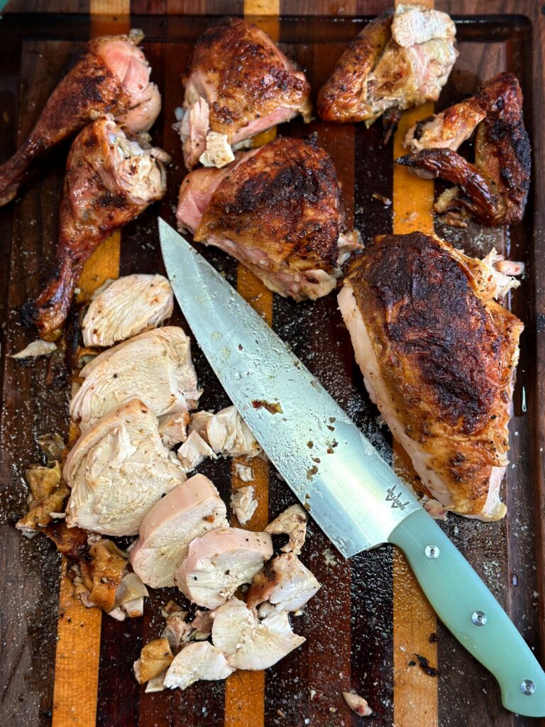 Smoked spatchcock chicken broken down on the cutting board with a chef's knife.