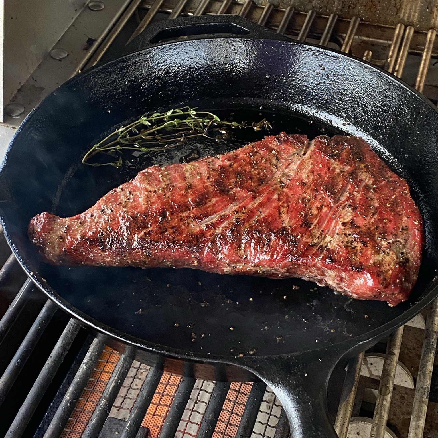 Tri tip getting seared in cast iron skillet with rosemary on the grill.